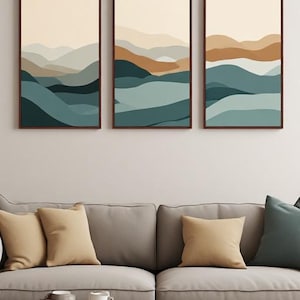 Op de afbeelding: Een set van drie verticale rechthoekige wandkunstprints met abstracte gelaagde landschapsontwerpen in tinten crème, beige, bruin, groenblauw en donkerblauw, elk in een dunne donkerbruine lijst en in een horizontale rij geplaatst.