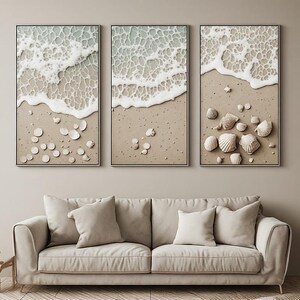 Peut inclure: Un triptyque composé de trois panneaux muraux verticaux représentant un rivage de plage sablonneuse avec de l'écume marine blanche recouvrant le sable et des coquillages éparpillés. L'œuvre présente des tons neutres beige, sable et blanc.