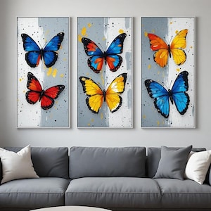 Peut inclure: Un ensemble de trois tableaux muraux verticaux sur fond gris clair avec des coups de pinceau blancs. Chaque toile présente deux papillons aux couleurs vives, notamment bleu, rouge, orange et jaune, agrémentés d'éclaboussures de peinture noire.