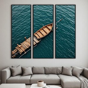 Peut inclure: Un ensemble d'art mural en triptyque présentant une vue en plongée d'une barque en bois amarrée à un ponton en bois patiné. La scène montre le bateau et le ponton flottant sur une eau bleu sarcelle profonde et ridée, divisée en trois panneaux.