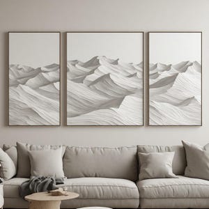 Puede incluir: Un conjunto de arte mural en tríptico que presenta tres impresiones enmarcadas de dunas de arena blanca abstractas. Cada impresión muestra líneas texturizadas y fluidas que imitan la apariencia de paisajes desérticos en tonos blanco roto, crema y gris claro.