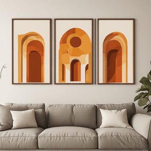 Könnte beinhalten: Ein Set aus drei gerahmten Wandbildern mit abstrakten architektonischen Torbogen-Designs in Terrakotta-, Rostorange- und Cremetönen. Jeder rechteckige Druck ist in einem dünnen, dunkelbraunen Rahmen gefasst und zeigt geometrische Formen.