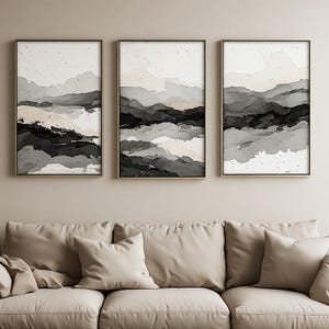 May include: A set of three rectangular wall art prints featuring abstract landscape designs in shades of black, grey, and cream. Each print is encased in a thin, light-coloured frame, displaying layered, fluid brushstrokes that mimic rolling hills.