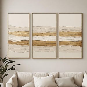 May include: A triptych wall art set featuring three vertical rectangular canvases framed in thin gold metal. Each canvas displays a textured abstract landscape with horizontal layers of cream, beige, and metallic gold paint applied in thick strokes.