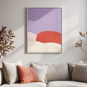 May include: A framed wall art print featuring an abstract composition of layered organic shapes in shades of light purple, soft pink, vibrant red, and cream, enclosed within a thin, light-coloured frame hanging on a plain wall.