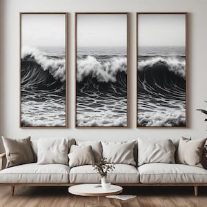 May include: A triptych of three vertical framed wall art prints featuring a black and white photograph of a large ocean wave crashing. Each frame is made of light-colored wood and displays a continuous view of the sea with white foam.