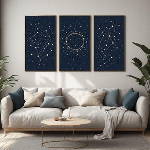 May include: A set of three rectangular wall art prints featuring dark navy blue backgrounds with gold-colored constellations and scattered stars. Each print is framed in a thin gold border, displaying celestial patterns of connected dots.