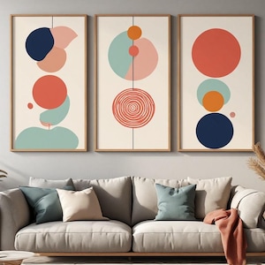 Puede incluir: Un conjunto de tres láminas de arte mural verticales en marcos de madera, cada una con fondo crema y formas geométricas abstractas en azul marino, coral, naranja y verde salvia, incluyendo círculos y un patrón en espiral sobre una línea.