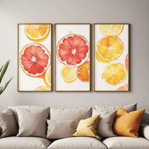Peut inclure: Un ensemble de trois impressions murales verticales dans de fins cadres dorés, chacune présentant des illustrations à l'aquarelle de tranches d'agrumes, oranges, pamplemousses et citrons, dans des tons jaune vif, orange et rose foncé sur fond blanc.