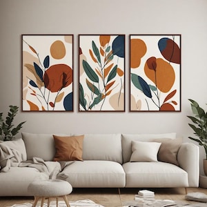 Peut inclure: Un ensemble de trois cadres muraux présentant des illustrations botaniques abstraites avec des formes organiques et de fines lignes noires. La palette de couleurs comprend des tons orange brûlé, bleu profond, vert sauge et crème sur fond clair.