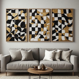 Peut inclure: Un triptyque composé de trois tableaux rectangulaires dans des cadres en bois clair, présentant chacun un motif en damier ondulé et déformé en noir, blanc et or métallique. L'œuvre est exposée au-dessus d'un canapé gris clair à quatre coussins.