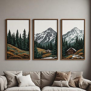 May include: A set of three vertical framed wall art prints depicting a continuous mountain landscape. The scene features snow-capped peaks, dense dark green pine forests, golden-brown grassy slopes, and a small wooden cabin nestled in the trees.