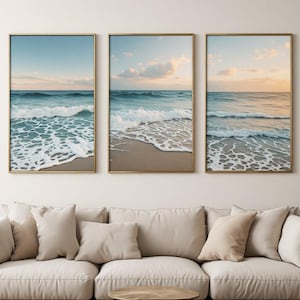 Può includere: Un trittico di tre stampe artistiche verticali da parete in sottili cornici dorate, ognuna delle quali mostra una scena oceanica continua con onde blu, schiuma marina bianca e rive sabbiose sotto un cielo tenue al tramonto con nuvole.