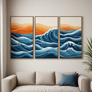 Può includere: Un set di trittici da parete composto da tre stampe rettangolari incorniciate. L'opera raffigura una scena oceanica stilizzata con onde blu stratificate, schiuma di mare bianca e colline arancioni sullo sfondo, racchiuse in cornici di legno.