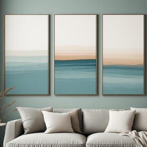 Peut inclure: Un ensemble de trois cadres muraux verticaux dorés fins, chacun présentant un motif de paysage abstrait en couches avec des bandes horizontales de crème doux, de pêche atténué et de diverses nuances de bleu sarcelle, créant un effet d'horizon.