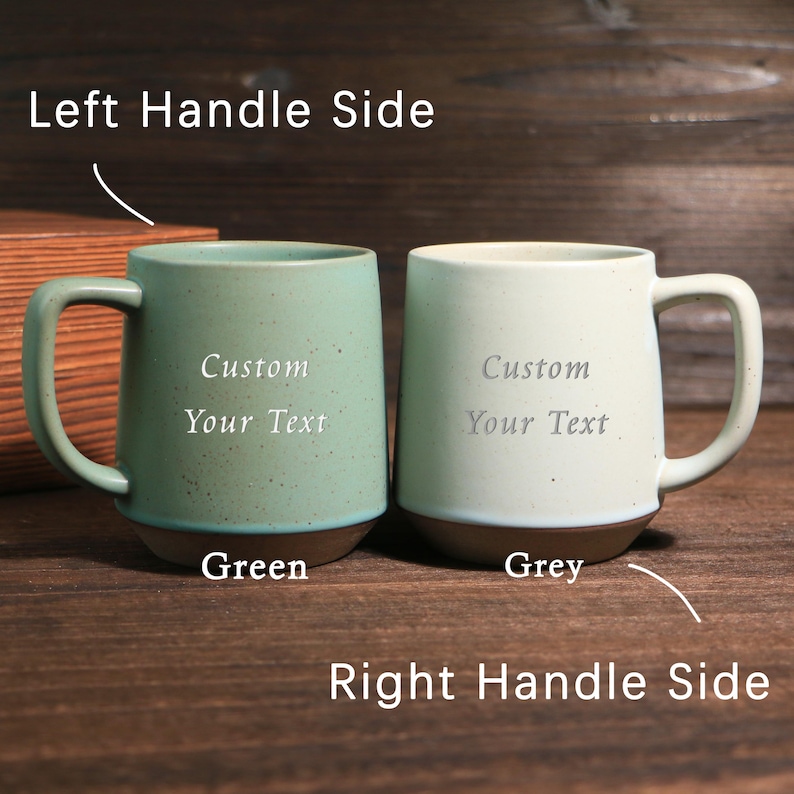 May include: Two ceramic mugs, one green and one grey, with brown bases and large handles. Each mug has the words "Custom Your Text" printed on the front. The mugs are displayed on a wooden surface.