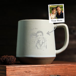 May include: A cream-coloured ceramic mug with a speckled finish and a dark brown base. The mug features a custom line-art engraving of a man and a boy, with the text "Daddy & Ben" above the illustration. A small inset photo shows the original image.