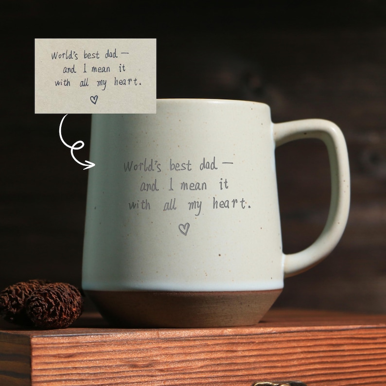 May include: Cream-colored ceramic mug with a brown base and a large handle. The mug is inscribed with the words "World's best dad - and I mean it with all my heart." A small heart symbol is below the text.