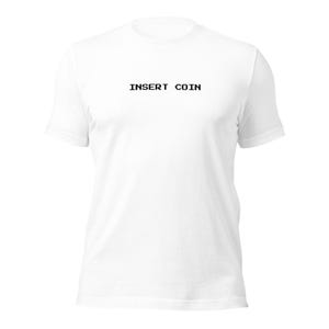 Puede incluir: Camiseta blanca con la frase "INSERT COIN" en negro impresa en el centro. La camiseta tiene mangas cortas y cuello redondo. La tela parece suave y ligera, adecuada para uso diario.