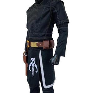 May include: A black long-sleeved tunic and pants set featuring a high collar, quilted shoulder detailing, and white stitching. A brown utility belt with a gold buckle and two attached pouches sits at the waist, alongside a white Mythosaur emblem.