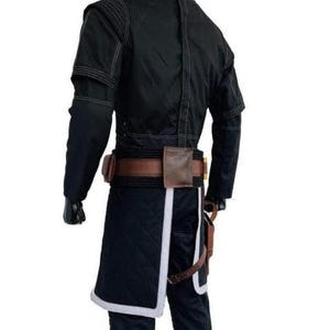 May include: A black long-sleeved jacket with visible stitching, paired with a brown leather utility belt featuring pouches. The outfit includes a black quilted skirt-like panel with a white border, worn over black trousers with a brown holster strap.