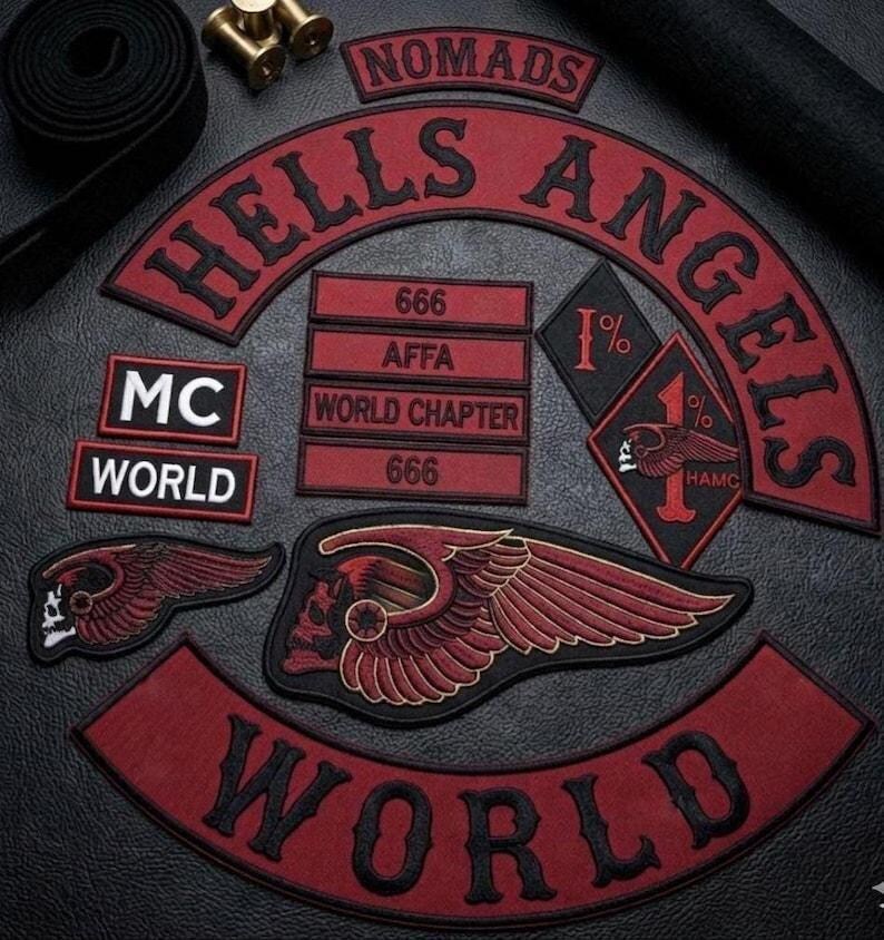 May include: A collection of embroidered patches featuring the text HELLS ANGELS, NOMADS, MC, WORLD, AFFA, 666, and WORLD CHAPTER. The set includes a large winged skull emblem, a diamond-shaped 1% patch, and various rectangular and curved red and black labels.