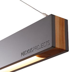 May include: A modern, rectangular pendant light fixture with a black metal frame and a wood accent. The light features a thin, white LED strip and the text "MICKUS PROJECTS" is engraved on the metal frame.