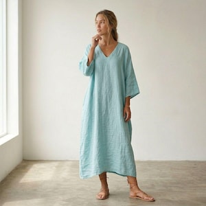 May include: A light blue, ankle-length dress with a V-neckline and three-quarter length sleeves. The garment features a loose, flowing silhouette and is crafted from a textured fabric. The dress is paired with brown strappy sandals.
