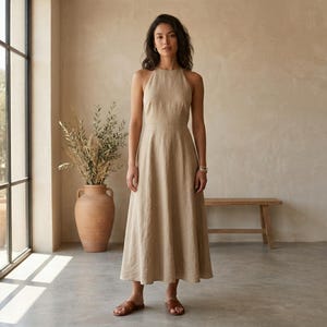 May include: A sleeveless, ankle-length beige dress with a high halter neckline and a fitted bodice that transitions into a flared, A-line skirt. The garment features a solid, neutral-toned fabric with visible texture and a clean, simple silhouette.
