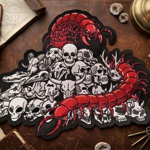 May include: Embroidered patch featuring a red centipede design crawling over a pile of white skulls and bones. The patch has a black border and is likely for jackets or bags. The design includes various skull types.