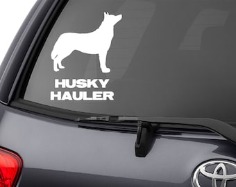 May include: White vinyl decal of a husky dog with the text "HUSKY HAULER" below it. The decal is on the rear window of a dark gray SUV. The vehicle has a Toyota emblem and the word "SEQUOIA" is visible.