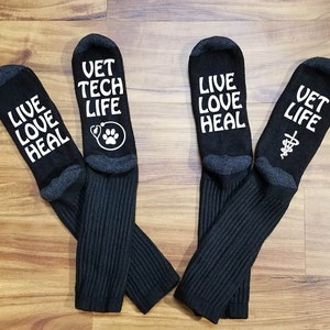 May include: Four pairs of black crew socks with white text. The socks have different sayings on them, including "Vet Tech Life", "Live Love Heal", and "Vet Life".