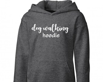 Op de afbeelding: Een donkergrijze hoodie met de tekst "dog walking hoodie" in witte letters met poot afdrukken.