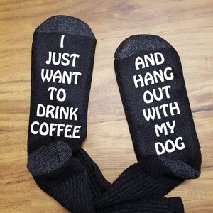 May include: A pair of black socks with white text. One sock says "I just want to drink coffee" and the other sock says "and hang out with my dog".