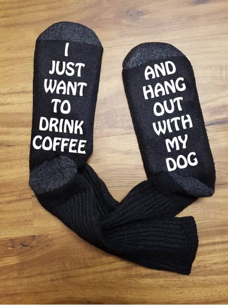 May include: A pair of black socks with white text. One sock says "I just want to drink coffee" and the other sock says "and hang out with my dog".