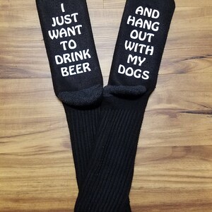 May include: A pair of black crew socks with white text. One sock says "I just want to drink beer" and the other says "And hang out with my dogs".
