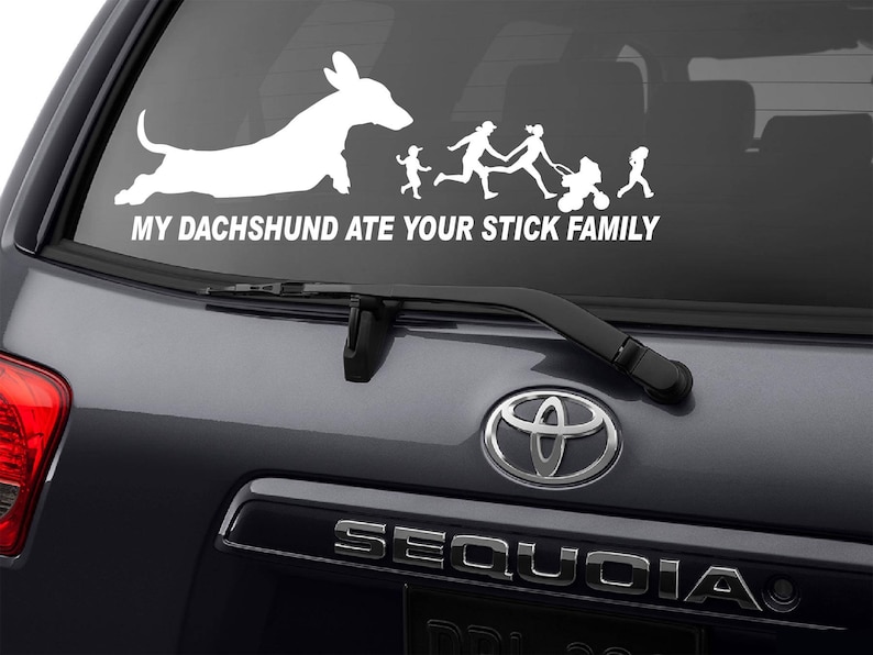 May include: A white vinyl decal sticker for a car window. The sticker shows a dachshund silhouette with the text "My Dachshund Ate Your Stick Family".