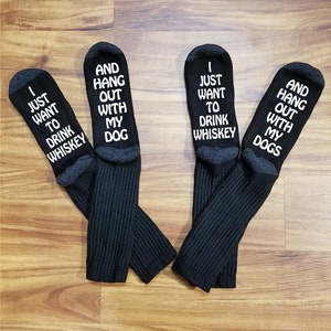 May include: Four black socks with white text. The socks have different sayings on them, including "I just want to drink whiskey", "And hang out with my dog", "I just want to drink whiskey", and "And hang out with my dogs".