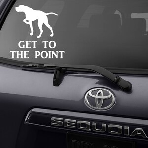 May include: White vinyl decal of a dog in a pointing pose, with the text "GET TO THE POINT" below. The decal is applied to the rear window of a dark gray SUV.