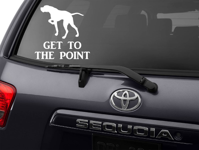 May include: White vinyl decal of a dog in a pointing pose, with the text "GET TO THE POINT" below. The decal is applied to the rear window of a dark gray SUV.