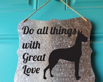 May include: A silver metal sign with a black silhouette of a dog and the text "Do all things with Great Love".