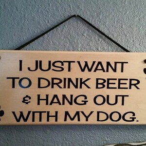 May include: Wooden sign with the text "I just want to drink beer & hang out with my dog."  The sign has black paw prints on each end.