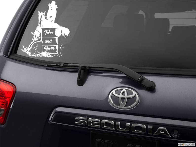 May include: White vinyl decal of a horse and rider jumping over a barrel with the text "Turn and Burn". The decal is on the back window of a gray SUV.