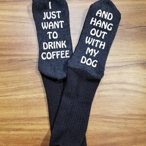 May include: A pair of grey socks with white text. One sock says "I just want to drink coffee" and the other sock says "And hang out with my dog".