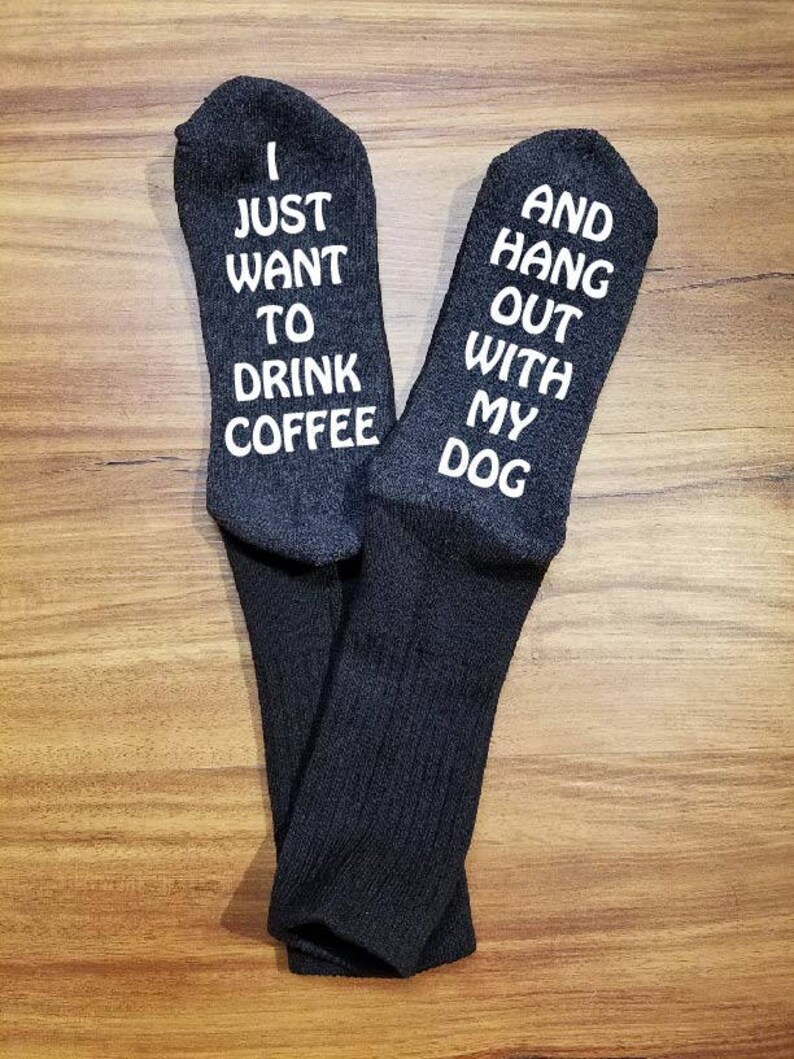 May include: A pair of grey socks with white text. One sock says "I just want to drink coffee" and the other sock says "And hang out with my dog".