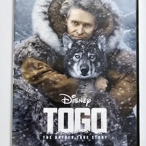 May include: DVD case for the Disney movie "Togo." The cover features Willem Dafoe and a husky dog in a snowy environment. The title "TOGO" is prominently displayed, with the tagline "The Untold True Story."