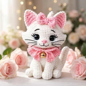 May include: A white crocheted cat plush toy featuring a pink yarn bow on its head and a matching pink crocheted collar with a small gold-colored bell attached at the center. The cat has large dark eyes, long black eyelashes, and a pink stitched nose.