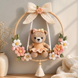 Può includere: Un orsetto all'uncinetto con vestito e fiocco color pesca siede su un'altalena a cerchio in legno. Il cerchio è decorato con fiori e foglie all'uncinetto nei toni del rosa, bianco e verde. Un grande fiocco color crema decora la parte superiore.