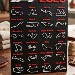 Pode incluir: Calendário de arte F1 impresso em 3D preto para a temporada de 2026. Apresenta contornos brancos de circuitos e o ano de 2026 em vermelho. Inclui circuitos como Portugal e Brasil.