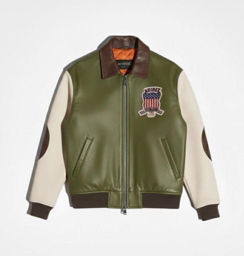 Op de afbeelding: Een olijfgroene jas met cr&egrave;mekleurige mouwen, een bruine leren kraag en bruine geribbelde boorden. De jas is voorzien van een ritssluiting aan de voorzijde, twee zijzakken en een geborduurde patch op de borst met de Amerikaanse vlag en tekst.